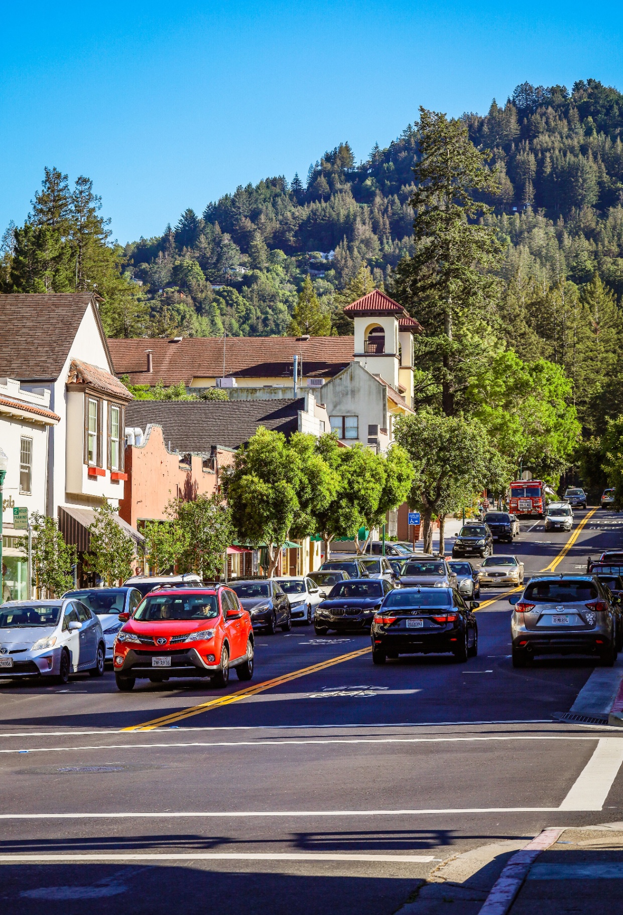 Sunny downtown Larkspur street lined with shops, parked cars, and redwood-covered hills in the distance